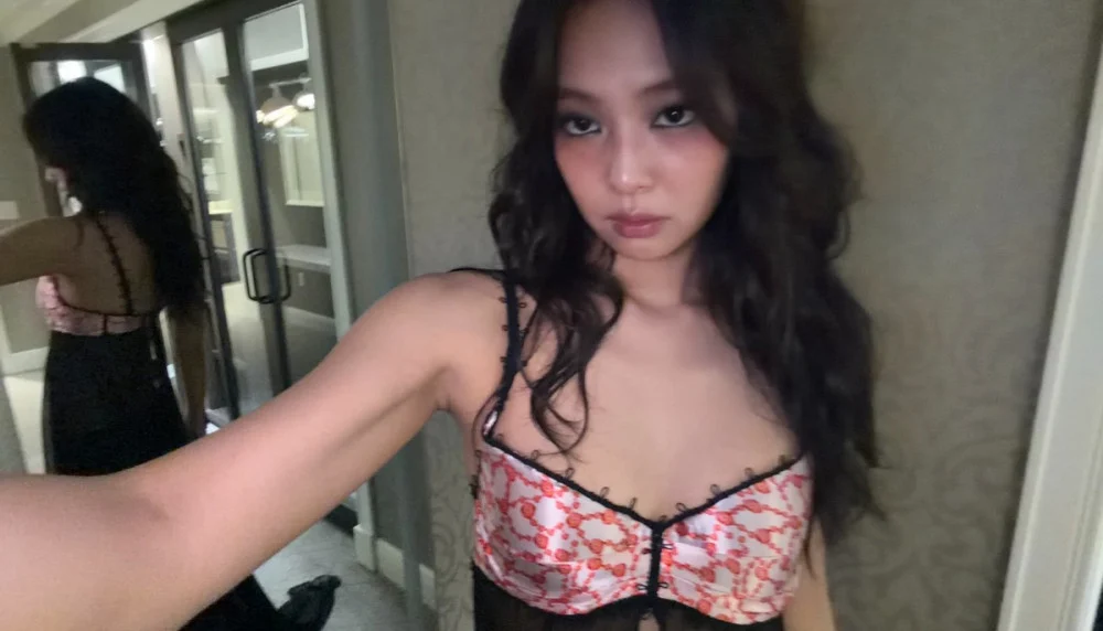 Jennie smiling onstage in glamorous performance outfit under bright lights